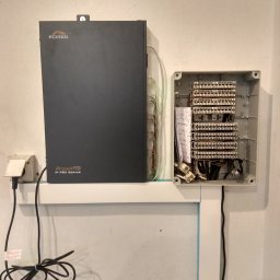 MT Systemy Marcin Taborek - Centrala telefoniczna Platan Proxima IP PBX Server zamontowana na ścianie obok skrzynki rozdzielczej z okablowaniem.