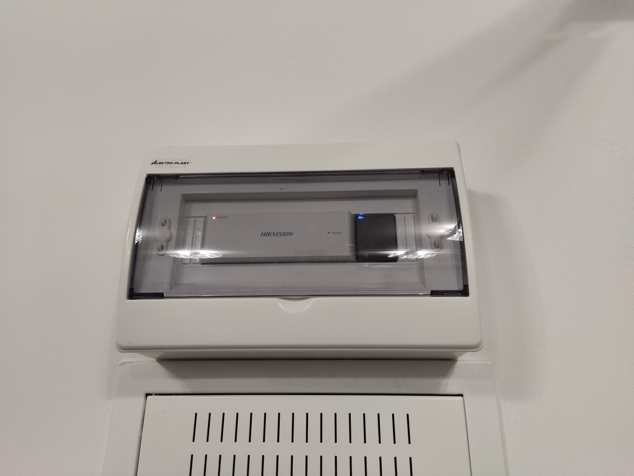 Zamknięta skrzynka z urządzeniem Hikvision w Radomiu, prawdopodobnie rejestrator monitoringu, z widocznymi diodami LED i przyciskiem reset.