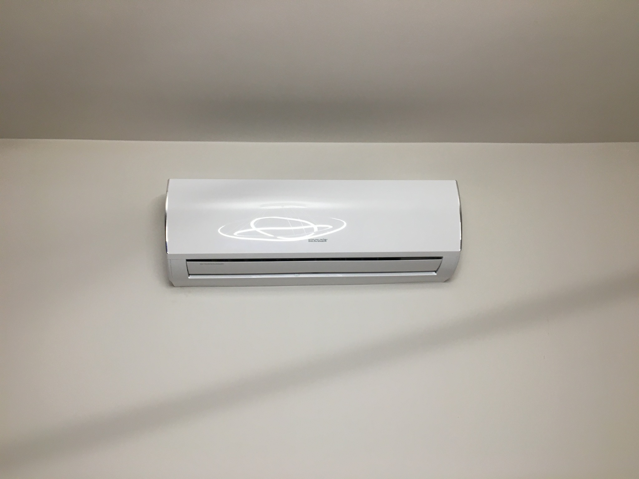 Biały klimatyzator Sinclair zamontowany na jasnej ścianie w Tomaszowie Mazowieckim, widoczne delikatne odbicie światła na obudowie.