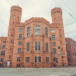 Neogotycki budynek sądu z cegły z dwiema wieżami zegarowymi, widoczny z poziomu ulicy z tramwajowymi torami.