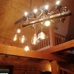 Rustykalny żyrandol z drewnianą belką i dekoracyjnymi żarówkami Edisona w drewnianym wnętrzu domu, widok od dołu.