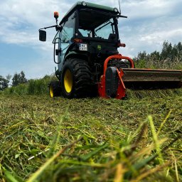 BIUREN Renata Pawlik - Zielony traktor John Deere z kosiarką rotacyjną na polu po skoszeniu trawy. Widoczne ślady cięcia i resztki trawy. Niebieskie niebo w tle.