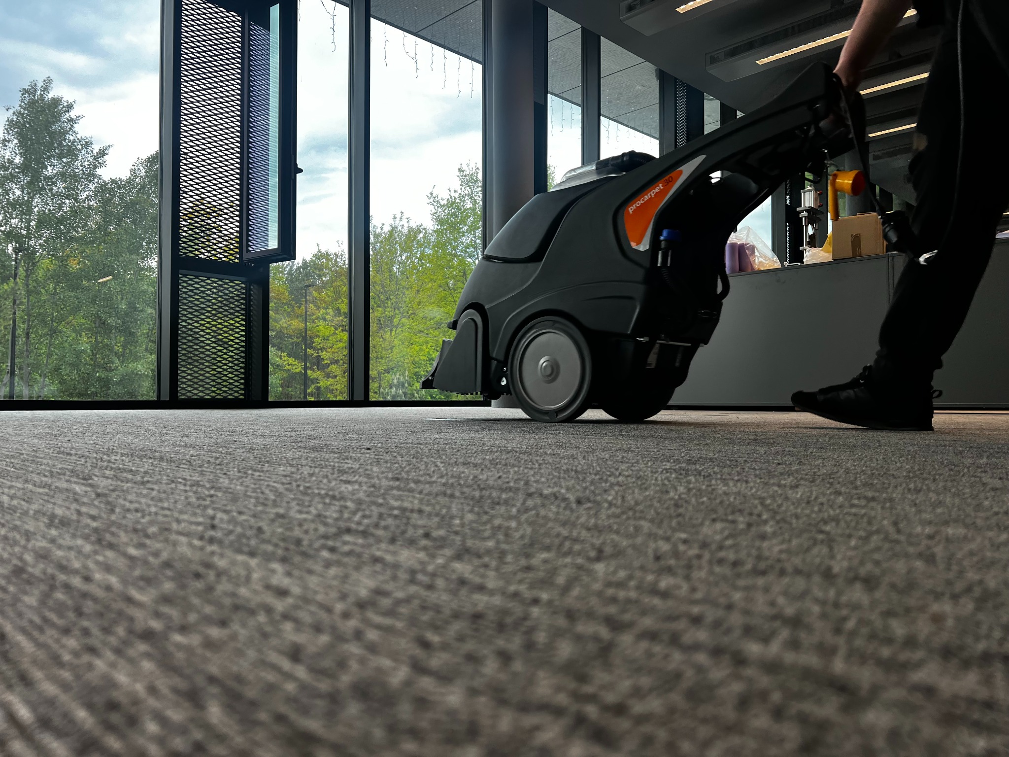 Profesjonalne czyszczenie wykładziny biurowej przy użyciu specjalistycznego odkurzacza piorącego Procarpet 30, z widokiem na zieleń za oknem.