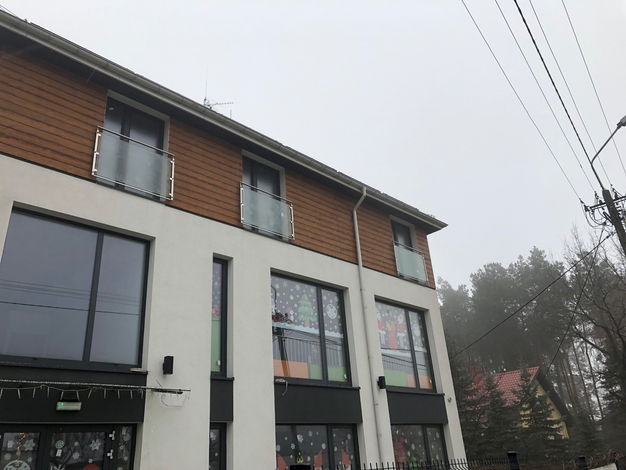 Nowoczesny budynek z drewnianą elewacją i balkonami z balustradami ze szkła i stali nierdzewnej, ozdobiony świątecznymi dekoracjami okiennymi.