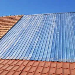 Fragment dachu z częściowo wymienionym pokryciem: blacha trapezowa w kolorze srebrno-niebieskim sąsiaduje z tradycyjną dachówką ceramiczną w odcieniach czerwieni i brązu, widoczne łączenia...