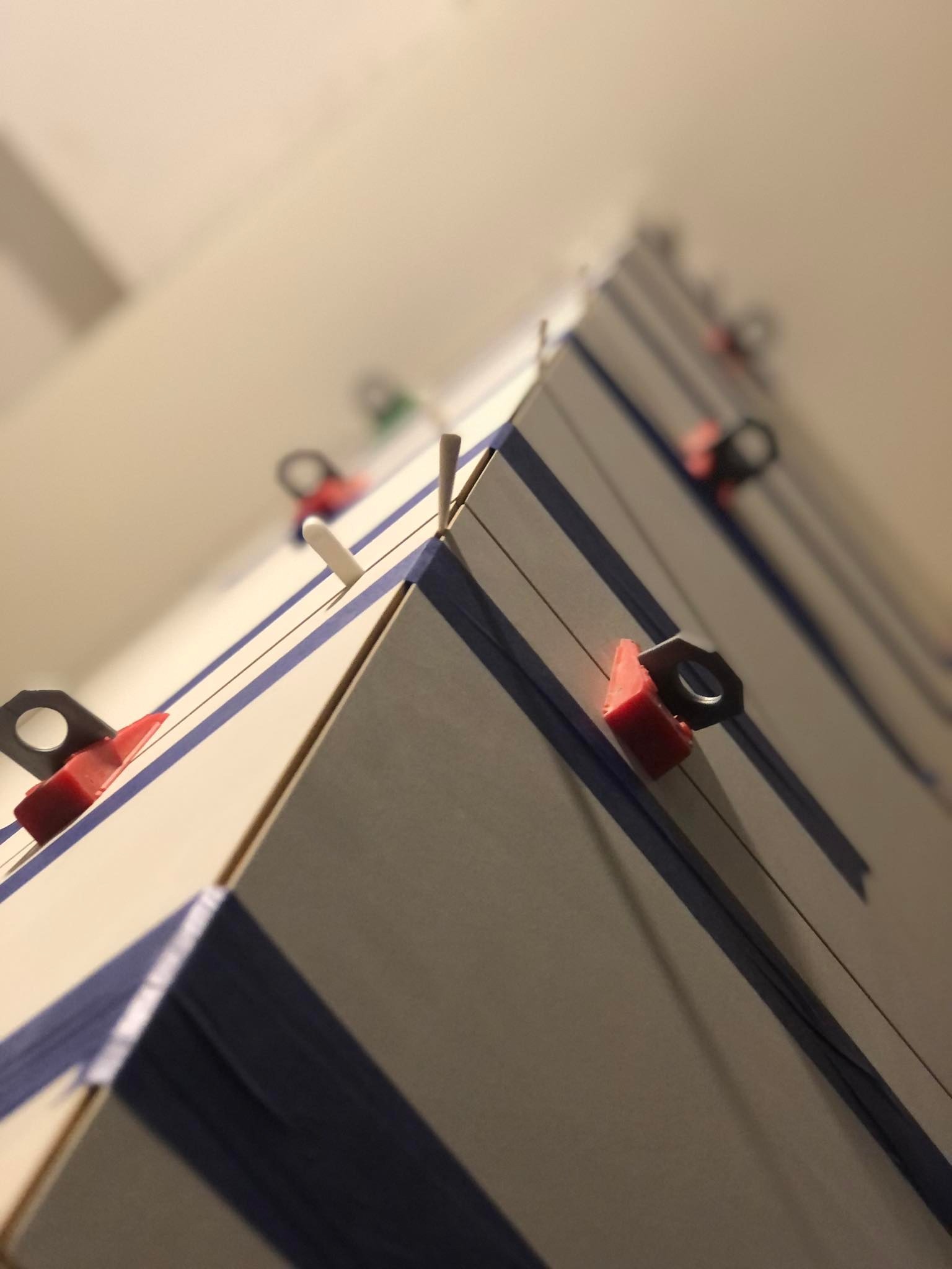 Niski kąt widzenia na świeżo ułożone płytki z niebieskimi paskami i systemem poziomowania płytek, w tym czerwone kliny i czarne zaciski, na tle jasnej ściany.