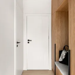 Nowoczesny przedpokój w Gdyni z drewnianą zabudową, siedziskiem i czarną torbą z motywem kwiatowym.