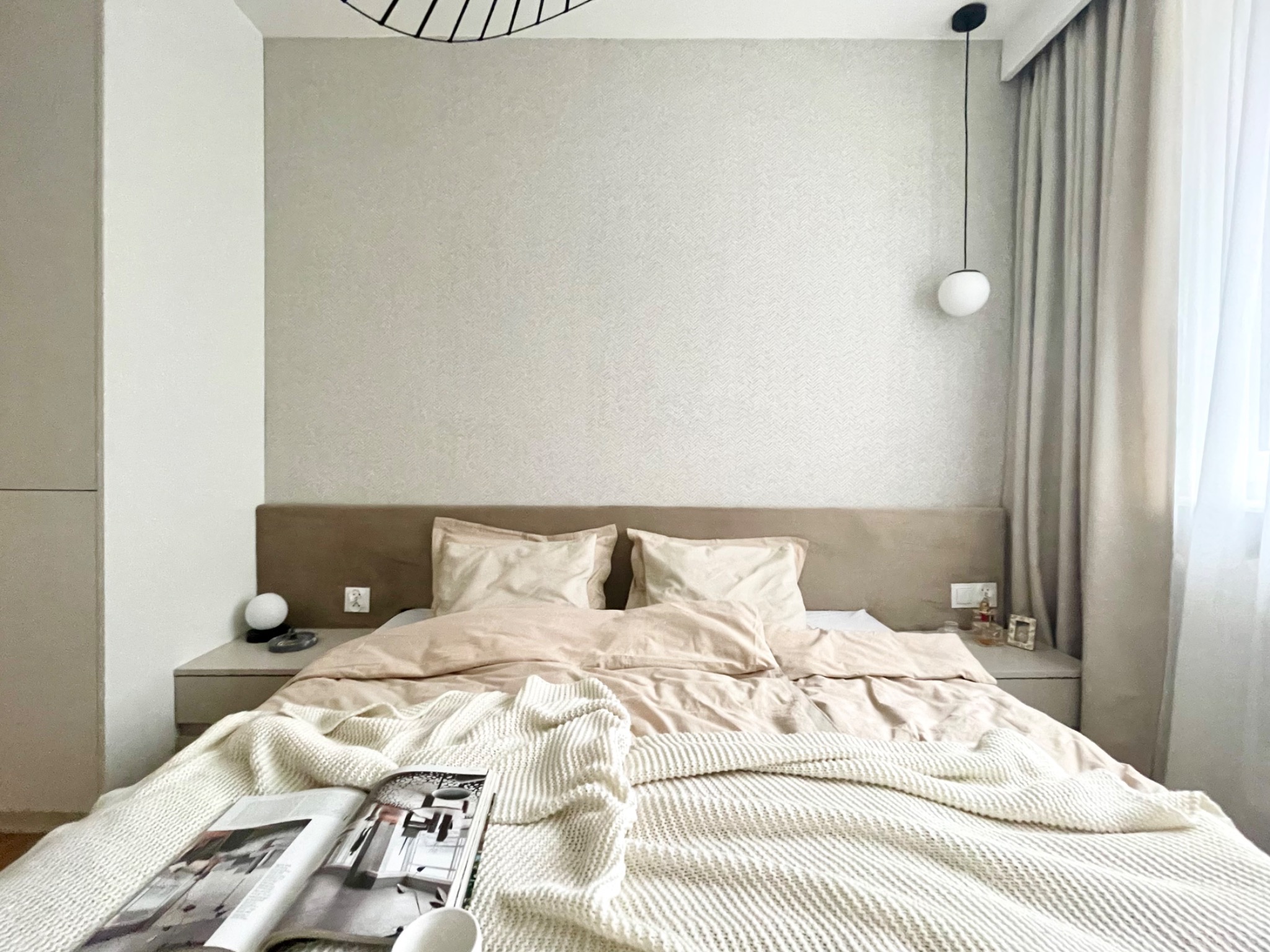 Neutralna sypialnia z beżową pościelą, lampką nocną i otwartym magazynem na łóżku, prezentująca minimalistyczny wystrój wnętrza.