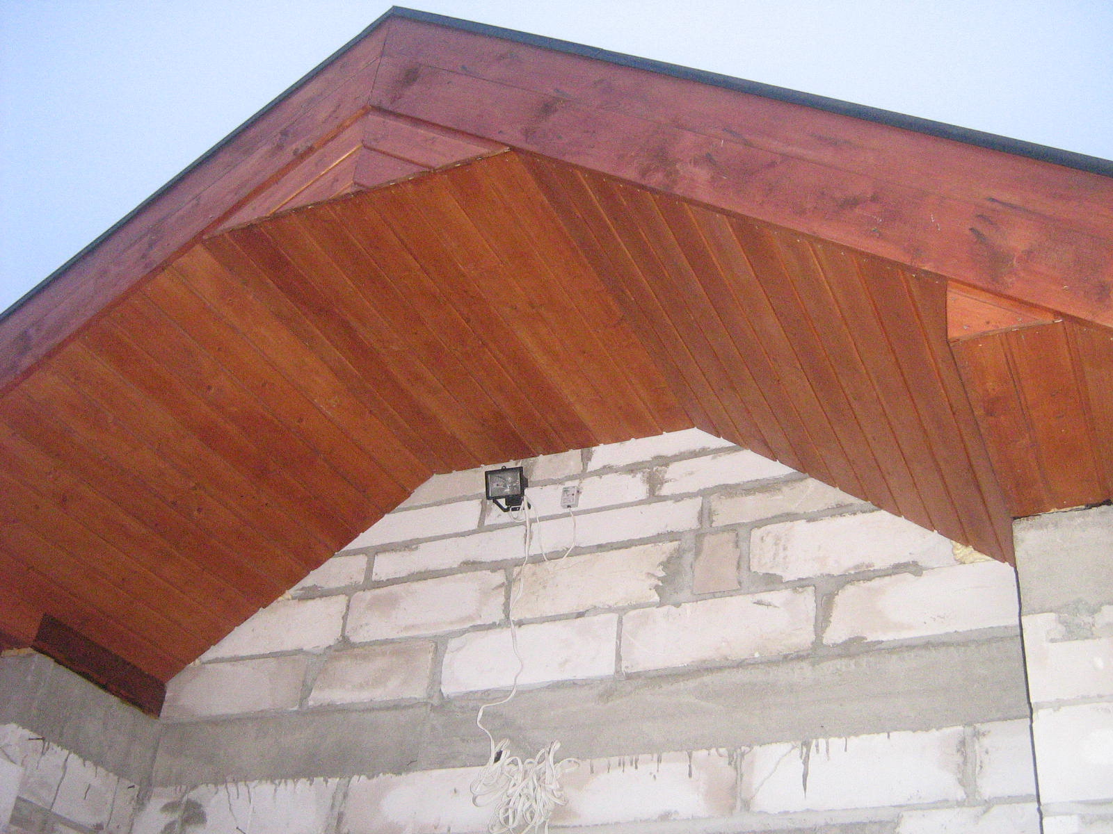 Drewniana podbitka dachowa w trakcie montażu, widoczne białe bloczki i wystające przewody elektryczne.