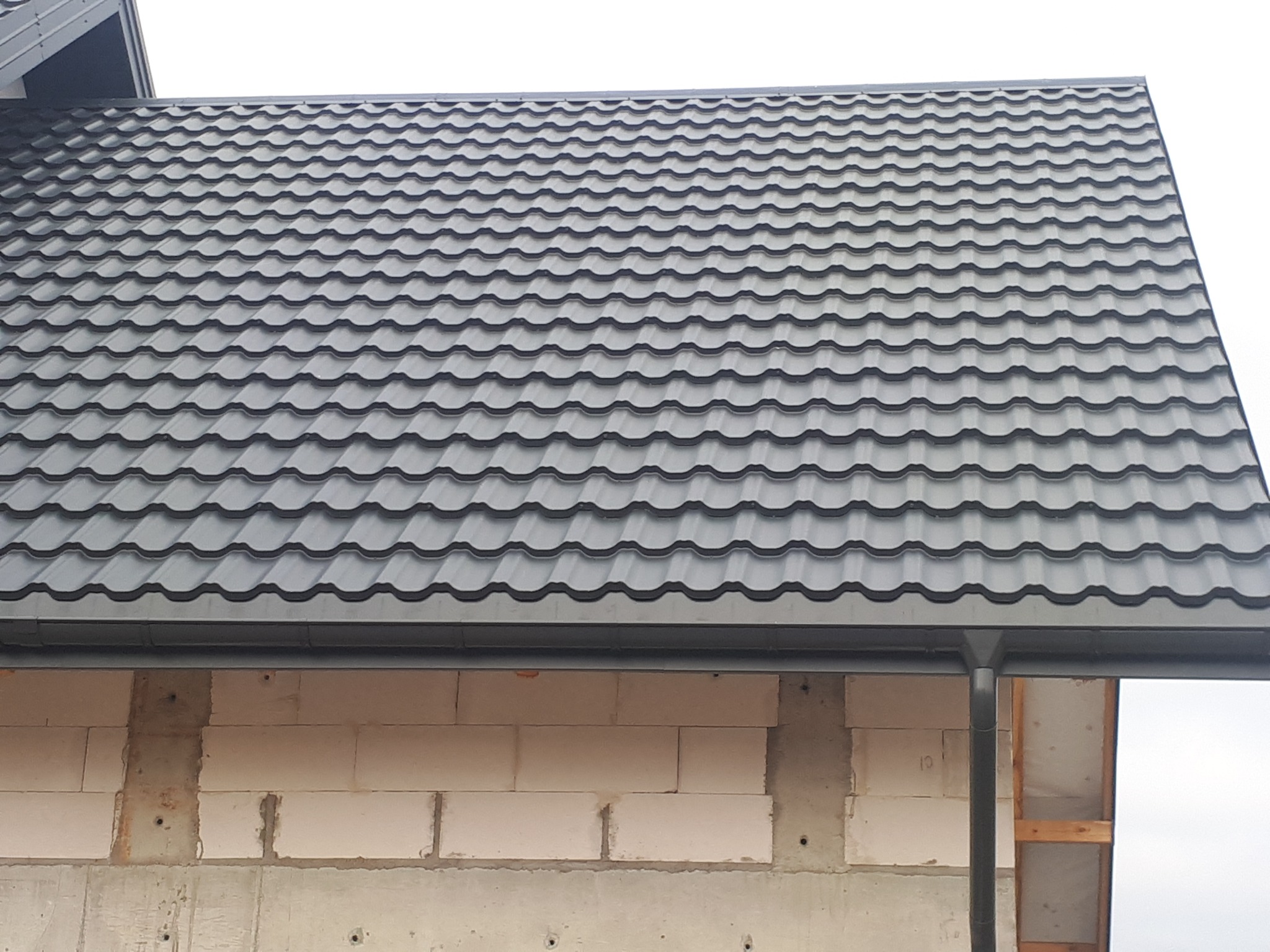 Szary dach z blachy trapezowej na budynku w trakcie budowy, widoczny fragment muru z betonu komórkowego i rynna.