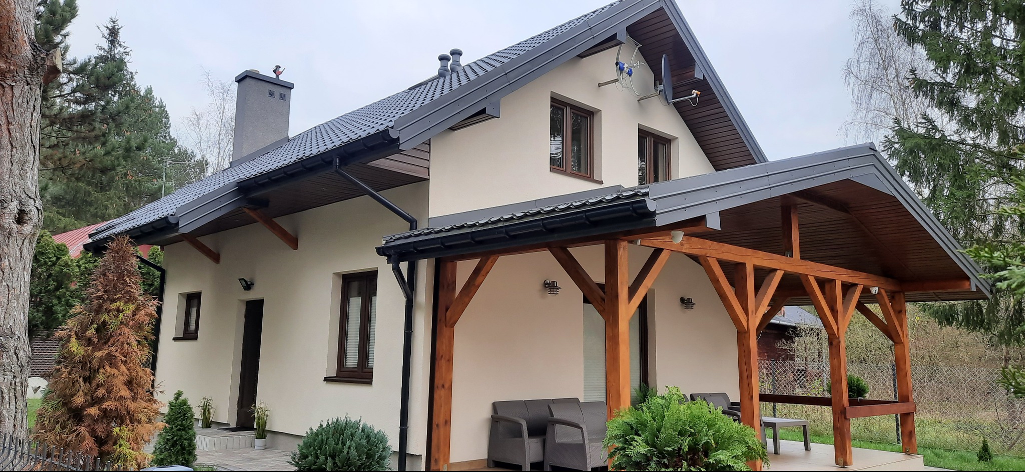 Dom jednorodzinny w Laskowie z nowym, grafitowym dachem z blachy trapezowej, orynnowaniem w kolorze oraz drewnianą konstrukcją zadaszenia tarasu.