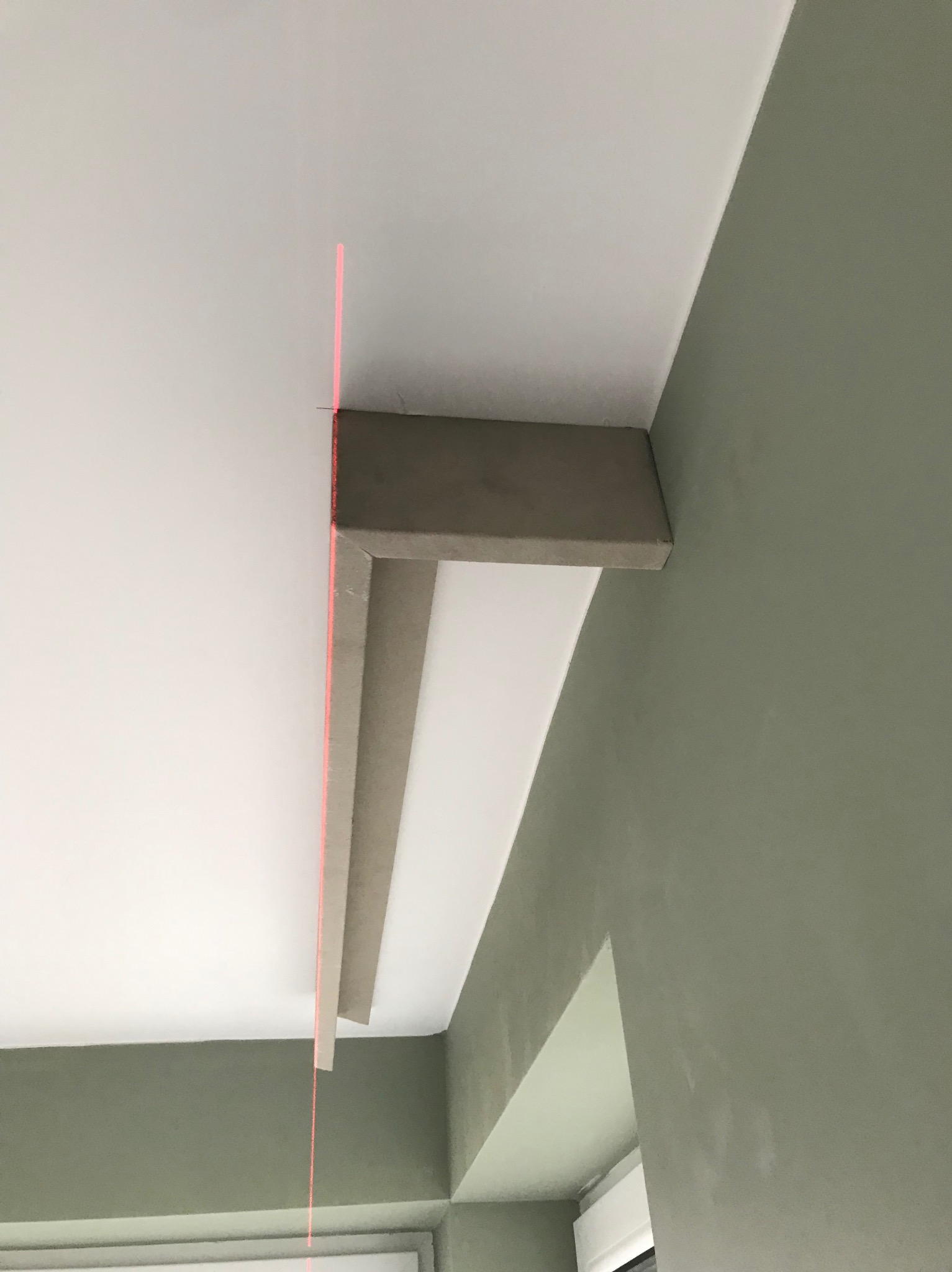 Zamontowana listwa sufitowa z płyty gipsowo-kartonowej, wyznaczona laserem na styku białego sufitu i oliwkowozielonej ściany. Widoczny fragment okna.