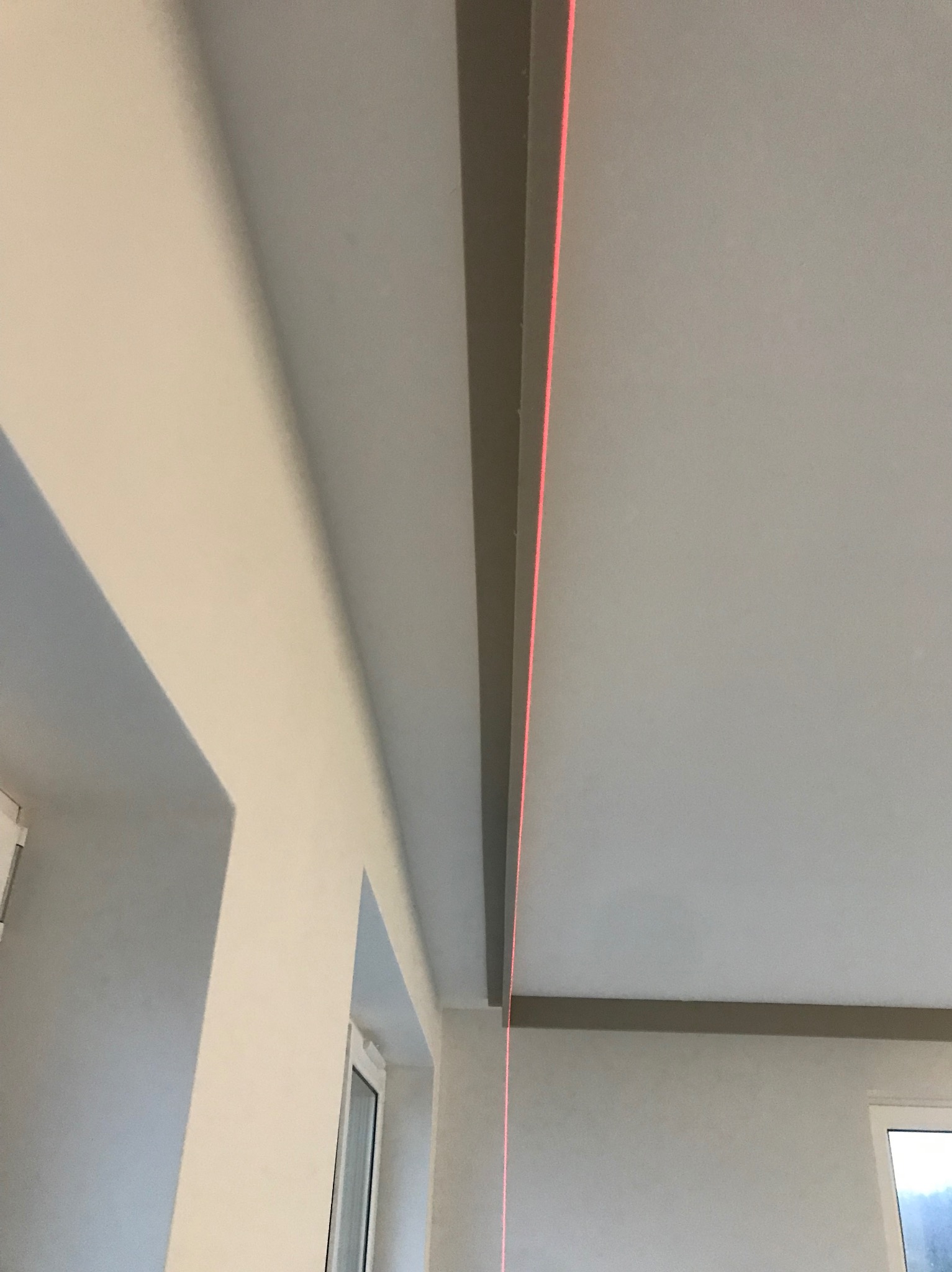 Wnętrze po remoncie z poziomowaniem sufitu za pomocą lasera. Widoczne listwy sufitowe i ściany pomalowane na jasny kolor. Czerwona linia lasera wyznacza poziom.