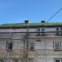 Budynek mieszkalny w trakcie prac dekarskich, widoczne rusztowania i fragment dachu pokrytego zieloną papą.