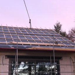 Express Dekarskie - Dach w trakcie wymiany: widoczna membrana dachowa, łaty, rusztowanie i fragment elewacji budynku w tle, wieczorne światło.