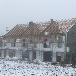 Express Dekarskie - Budowa domu w zimowy dzień: widoczna konstrukcja więźby dachowej, rusztowania i ocieplenie ścian zewnętrznych, dwóch robotników w jaskrawych spodniach na rusztowaniach.