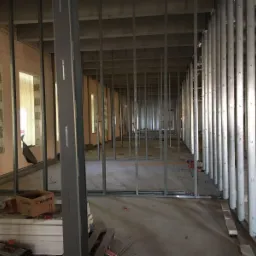 Wnętrze budynku w trakcie budowy, widoczne metalowe szkielety ścian działowych, częściowo obłożone płytami, z narzędziami i pudełkiem Wurth na pierwszym planie.