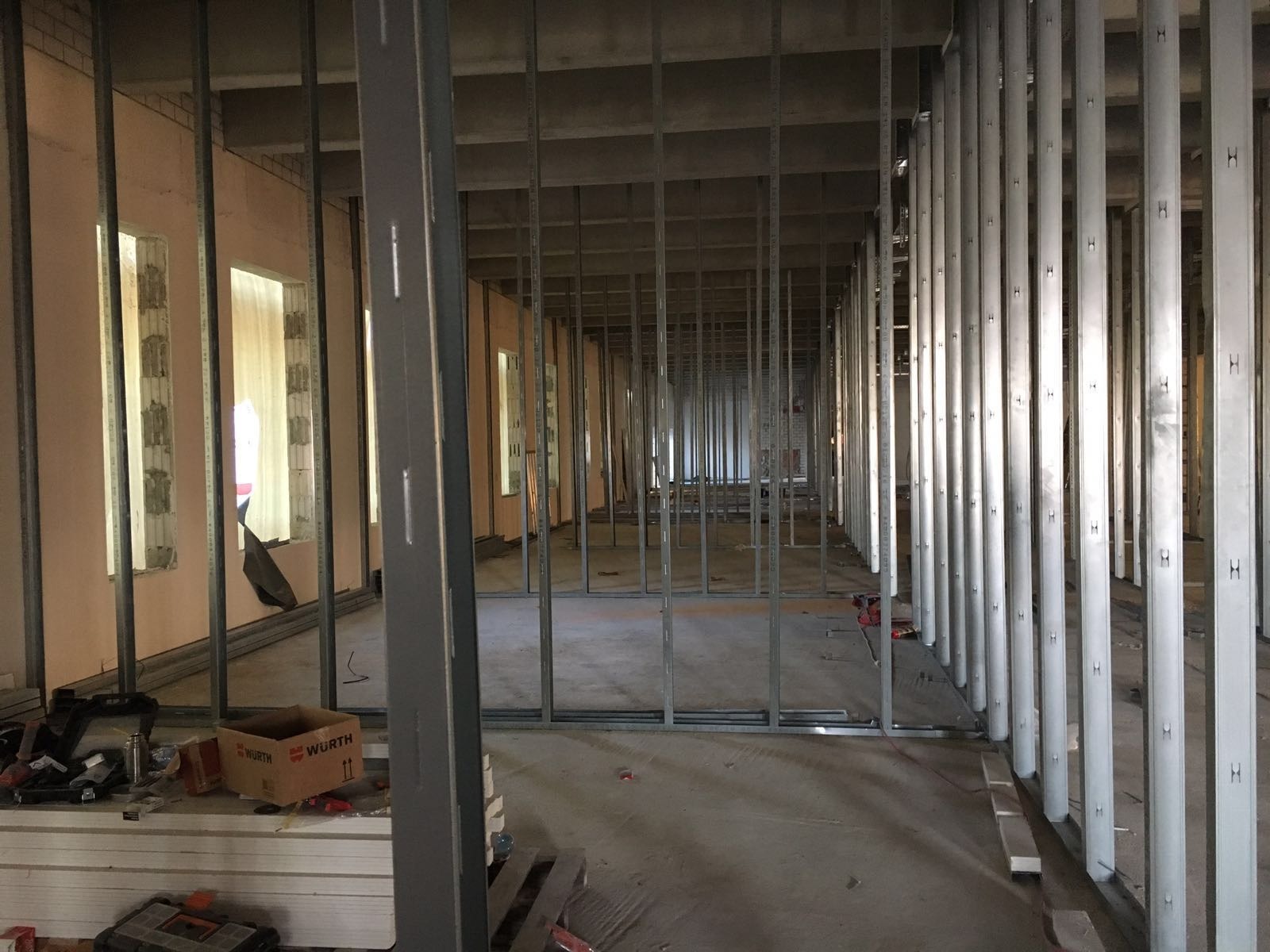 Wnętrze budynku w trakcie budowy, widoczne metalowe szkielety ścian działowych, częściowo obłożone płytami, z narzędziami i pudełkiem Wurth na pierwszym planie.