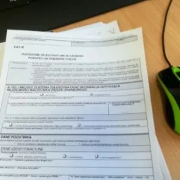 Formularz VAT-R, Zgłoszenie rejestracyjne w zakresie podatku od towar&oacute;w i usług, leżący na biurku obok klawiatury i myszki komputerowej. Dokument wypełniony częściowo, widoczne rubryki...