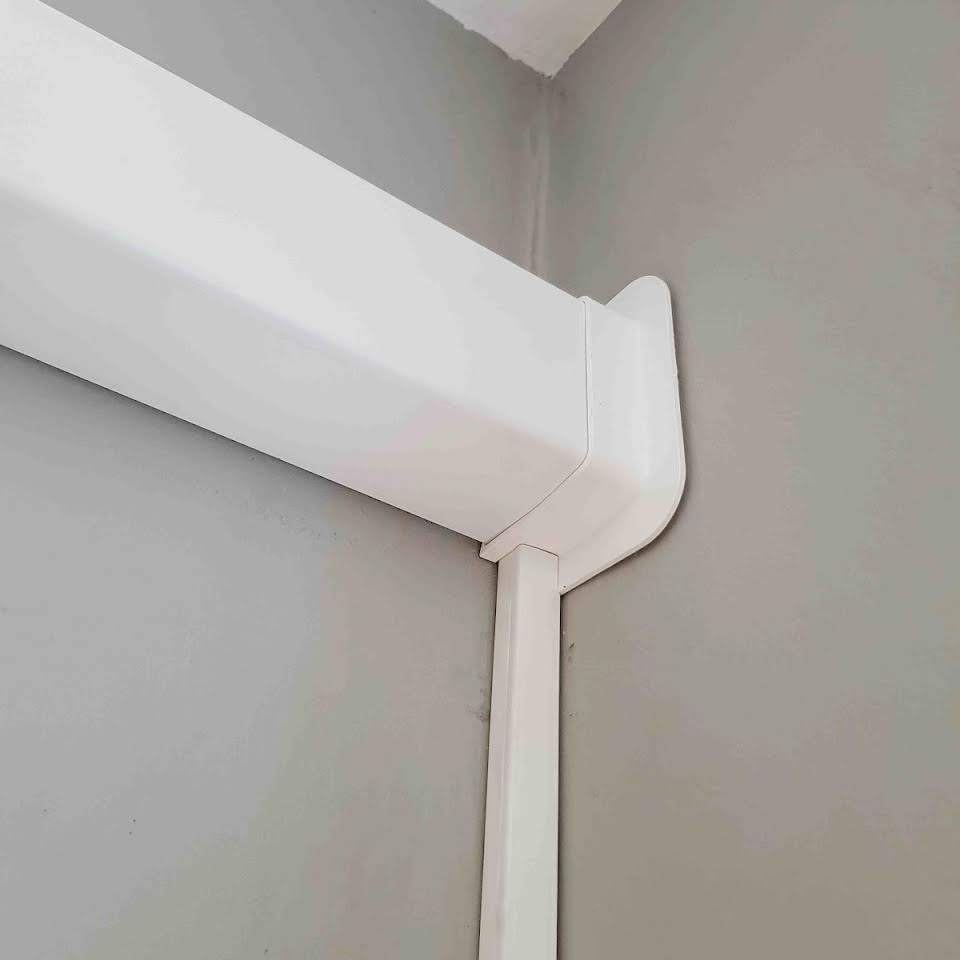 Biała listwa maskująca instalację klimatyzacji, przymocowana do szarej ściany w rogu pomieszczenia, widok z bliska.