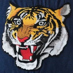 Wyhaftowana naszywka przedstawiająca głowę tygrysa z otwartym pyskiem, widoczne detale takie jak paski, zęby i faktura haftu, umieszczona na granatowym tle.