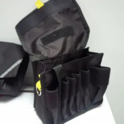 Czarny, otwarty organizer narzędziowy z wieloma przegródkami i żółtymi akcentami, widoczny na jasnym tle, obok torby kurierskiej również w czarnym kolorze.