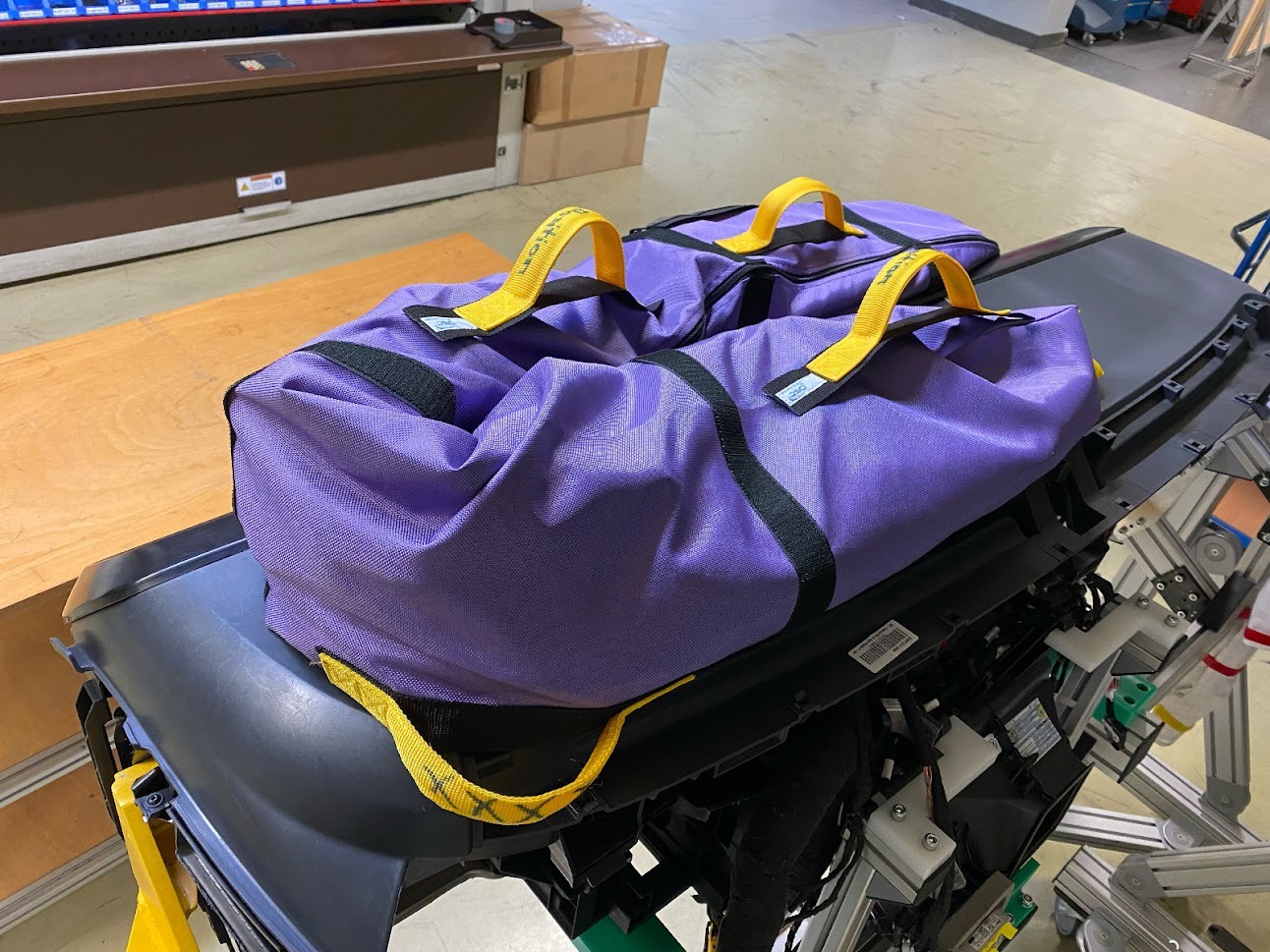 Dwie fioletowe torby z czarnymi paskami i żółtymi uchwytami leżące na czarnej platformie z widoczną konstrukcją metalową poniżej.