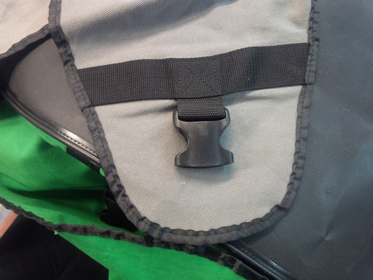 Fragment torby z szarego i czarnego materiału z zieloną podszewką i plastikowym zapięciem.