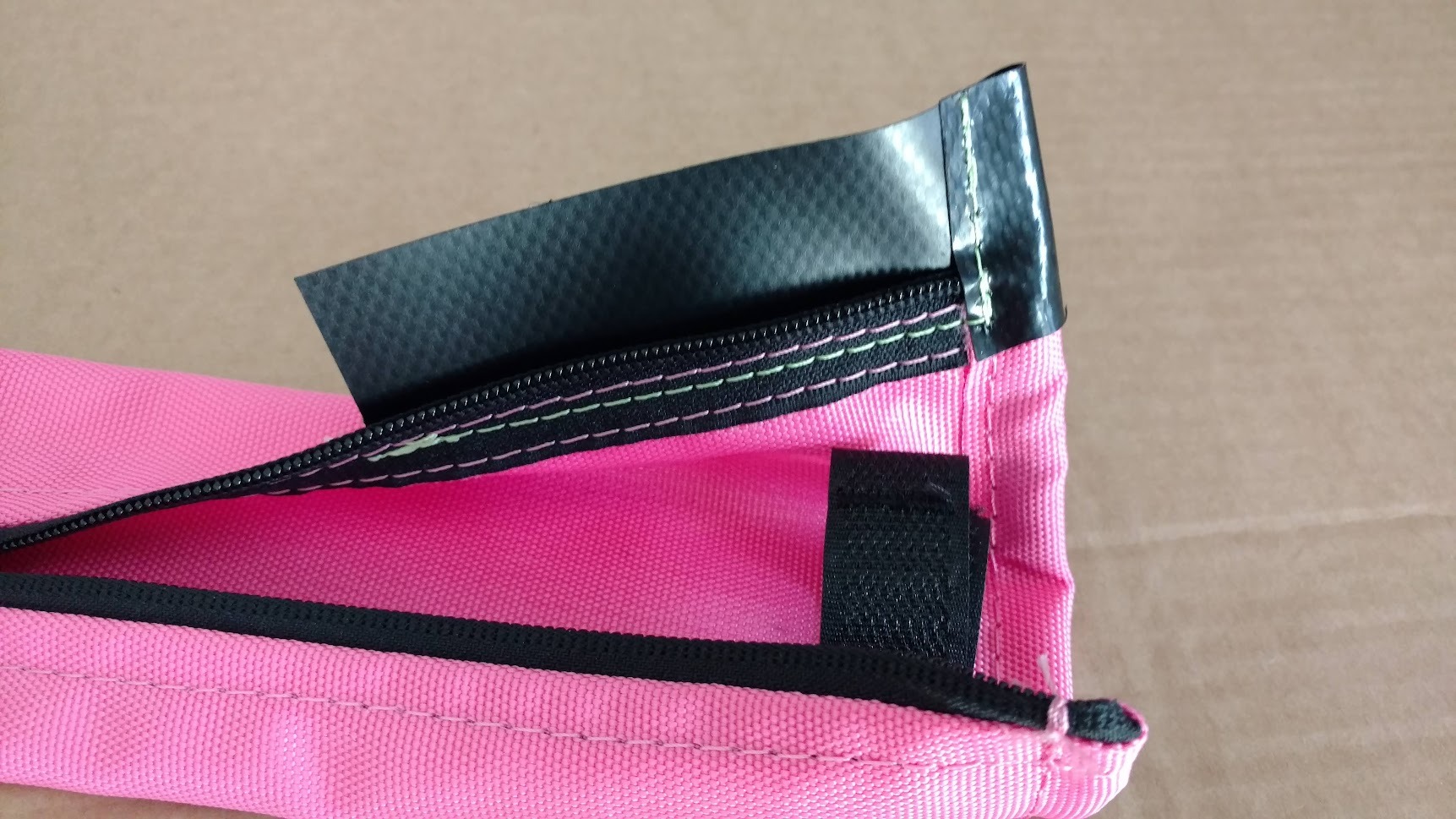 Różowy pokrowiec z czarnym zamkiem błyskawicznym, wzmocniony czarną taśmą, z widocznymi nićmi w kolorze zielonym i różowym.