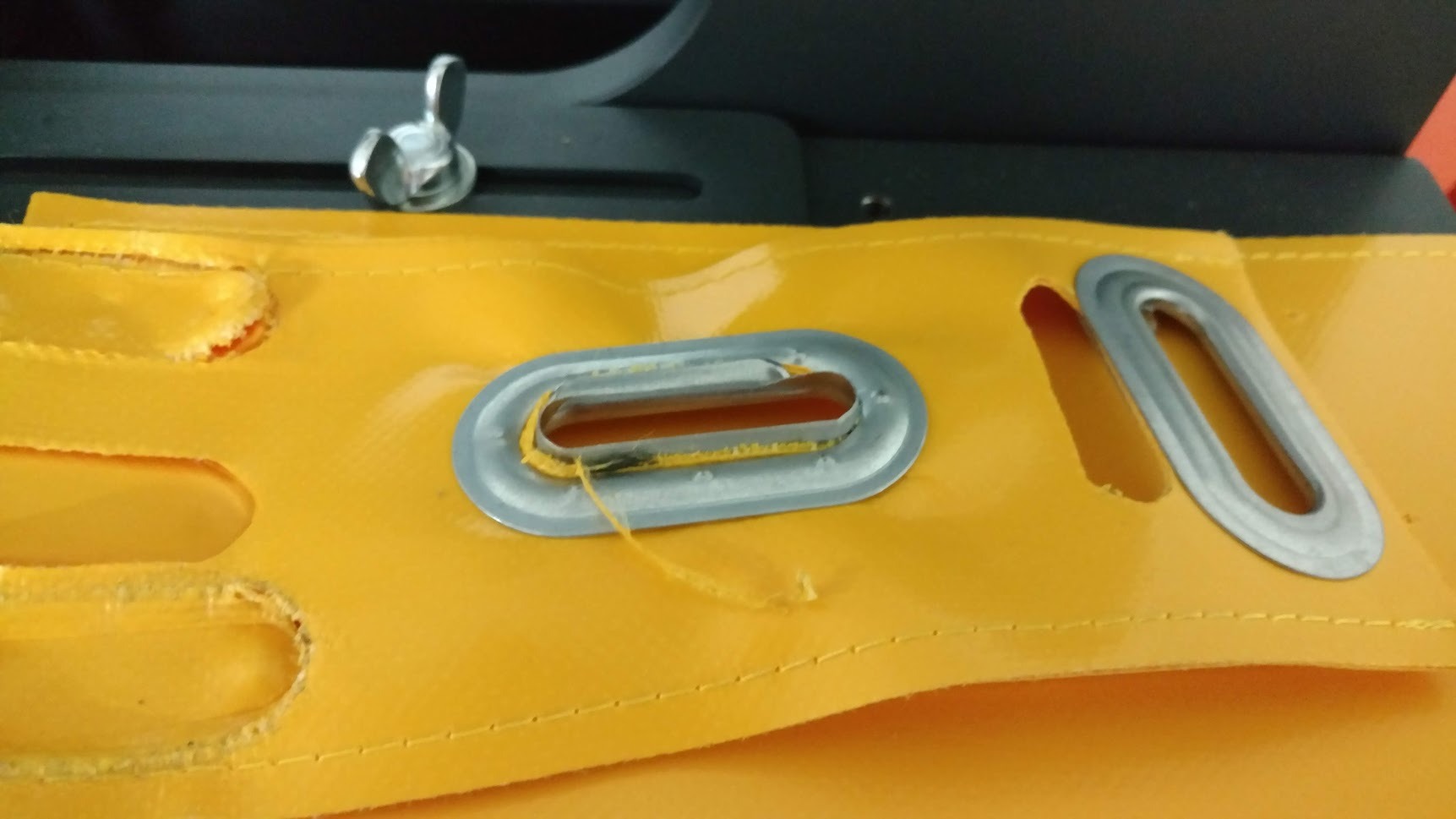 Żółty pokrowiec z tworzywa sztucznego z metalowymi oczkami, widoczne szwy i niedociągnięta nitka przy jednym z otworów.