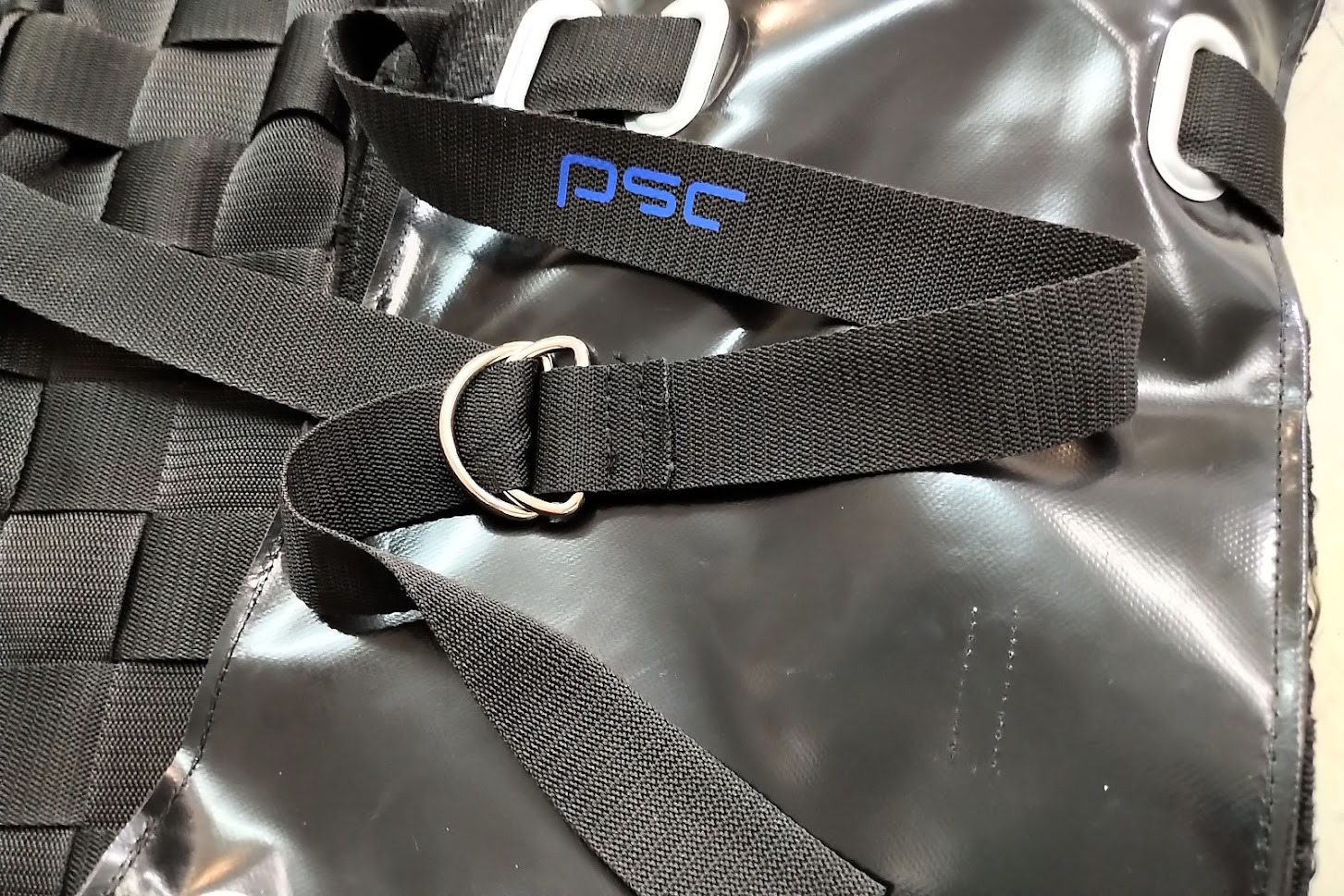 Czarny pokrowiec z pasami parcianymi, metalowymi kółkami i niebieskim napisem PSC, wykonany z błyszczącego materiału.