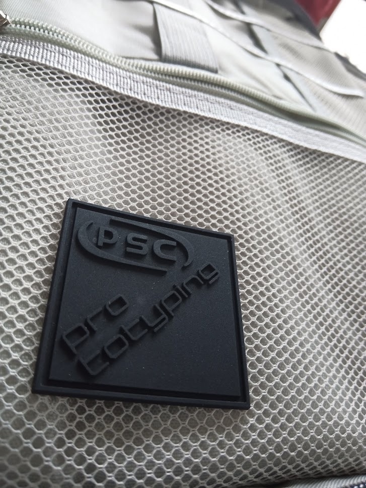 Szary pokrowiec z siatki z przyszytą czarną gumową naszywką z napisem 'PSC Prototyping'.