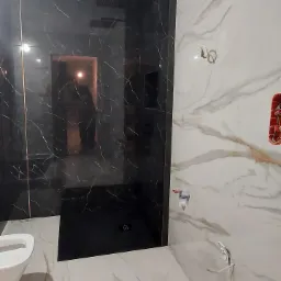 Nowoczesna łazienka z kabiną prysznicową typu walk-in wyłożoną czarnymi płytkami imitującymi marmur z złotymi żyłami, kontrastująca z białymi płytkami o marmurowym wzorze na pozostałych ścianach.