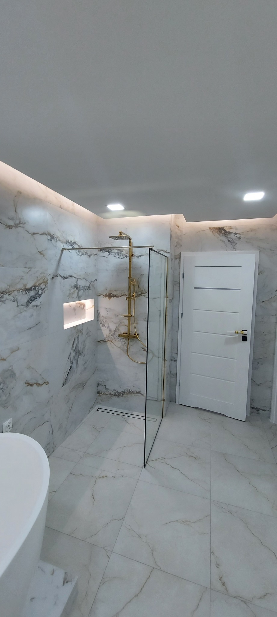 Elegancka łazienka z marmurowymi płytkami, złotą armaturą prysznicową i podświetlaną wnęką w ścianie.