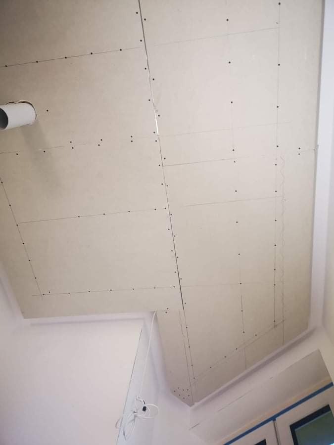 Sufit z zamontowanymi płytami gipsowo-kartonowymi, widoczne łączenia i wkręty, fragment instalacji wentylacyjnej w rogu.