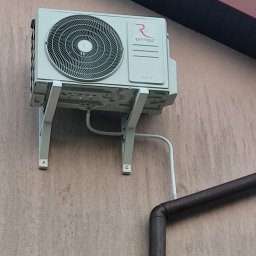 HYDROINSTAL-OZE Sławomir Łętocha - Zamontowana na elewacji zewnętrzna jednostka klimatyzacji Rotenso Hiro z widocznymi przewodami i rurą spustową. Ujęcie z dołu, lekko z prawej strony.