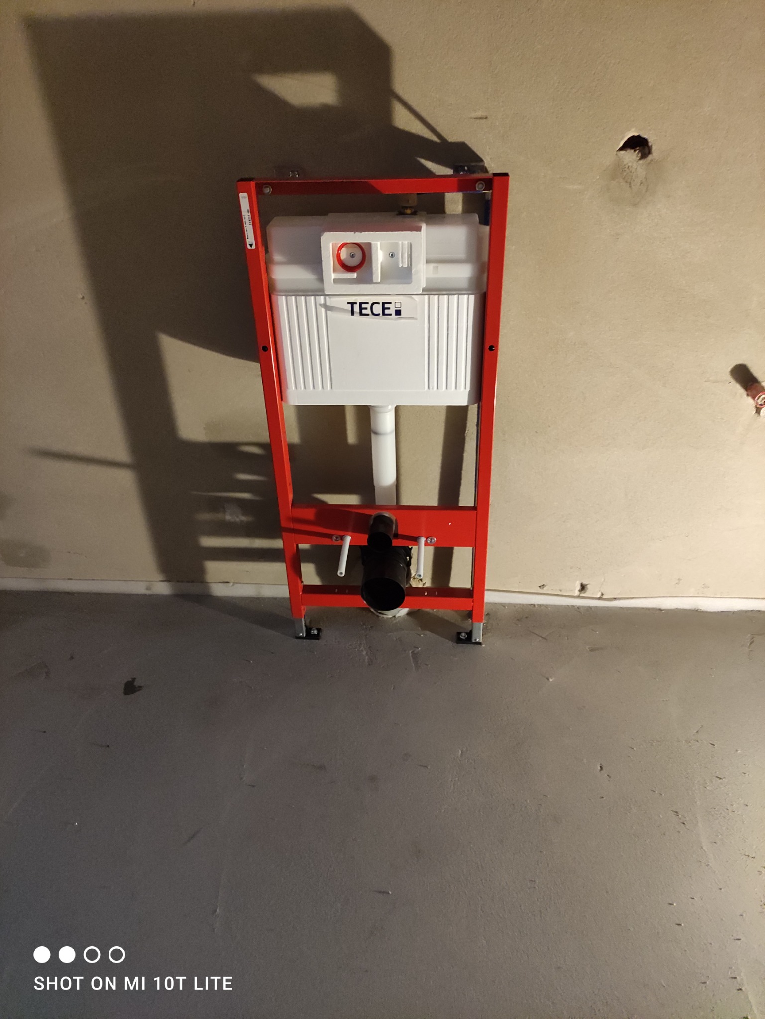 Stelaż podtynkowy z białą spłuczką TECE, zamontowany na surowej ścianie w trakcie prac hydraulicznych.