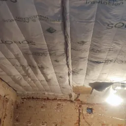 Montaż izolacji termicznej i akustycznej poddasza z widocznymi panelami SONOTIZ Thermal & Acoustic Insulation i fragmentem ściany z cegły