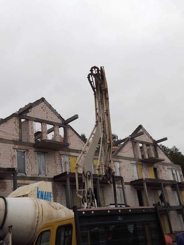 Surowy stan budynku wielorodzinnego z betonu komórkowego, z widocznym podnośnikiem do wylewania betonu i betoniarką z logo Knauf, w pochmurny dzień.