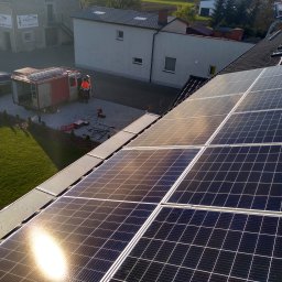 NLOOK SPÓŁKA Z OGRANICZONĄ ODPOWIEDZIALNOŚCIĄ - Montaż paneli słonecznych na dachu domu jednorodzinnego, widoczny samochód serwisowy i pracownicy w odblaskowych kamizelkach.