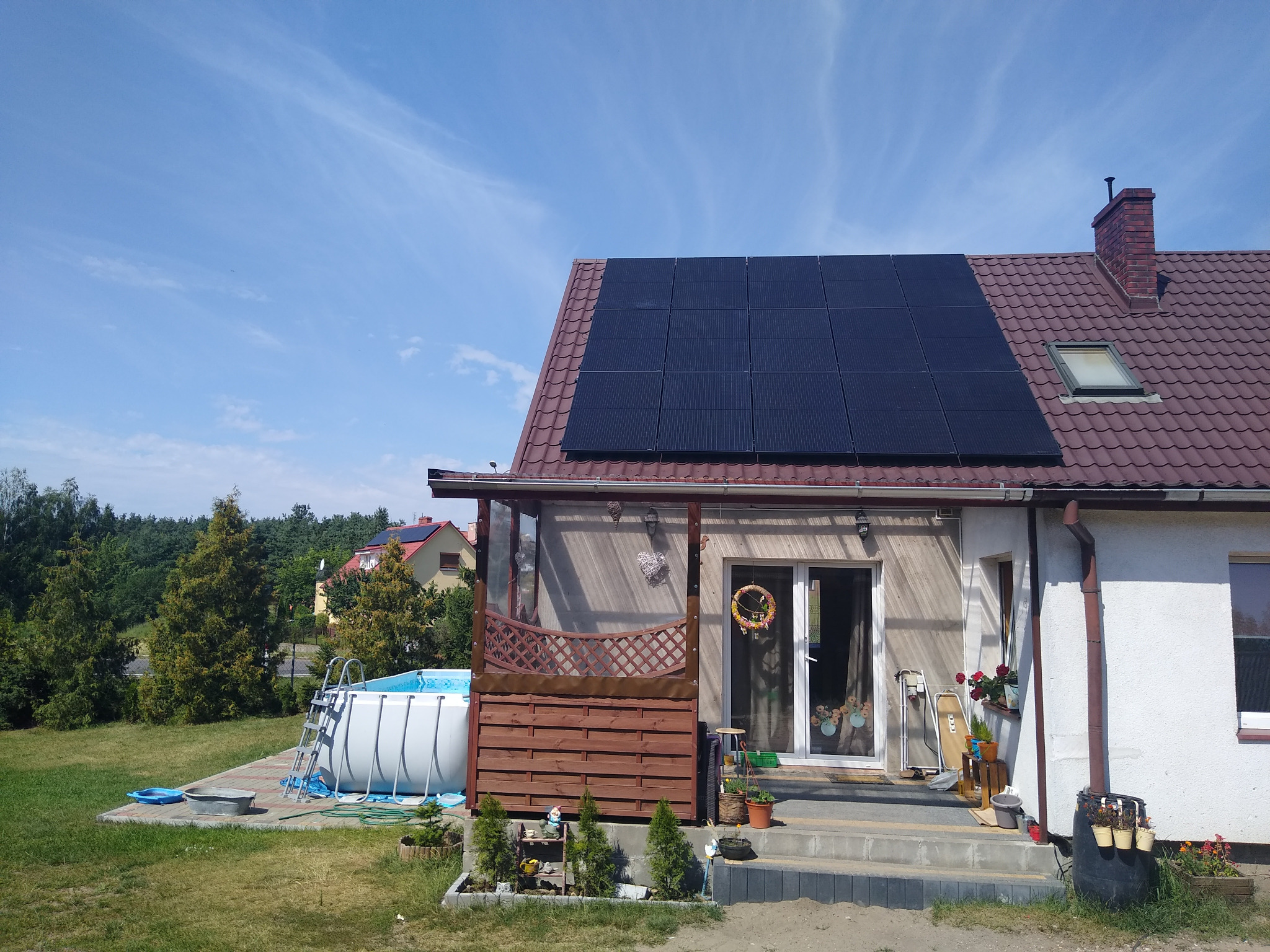 Dom jednorodzinny z zamontowanymi panelami słonecznymi na dachu, obok basen ogrodowy, widok z poziomu gruntu.