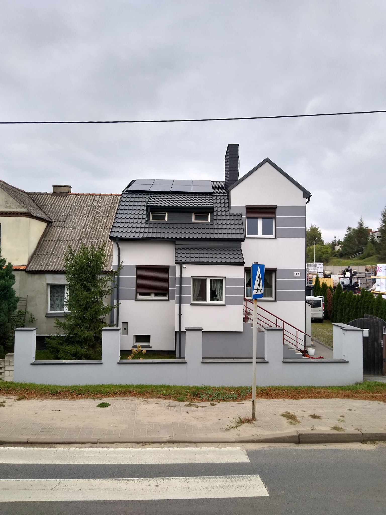 Dom jednorodzinny z panelami słonecznymi na dachu, widok z ulicy, znak przejścia dla pieszych na pierwszym planie.