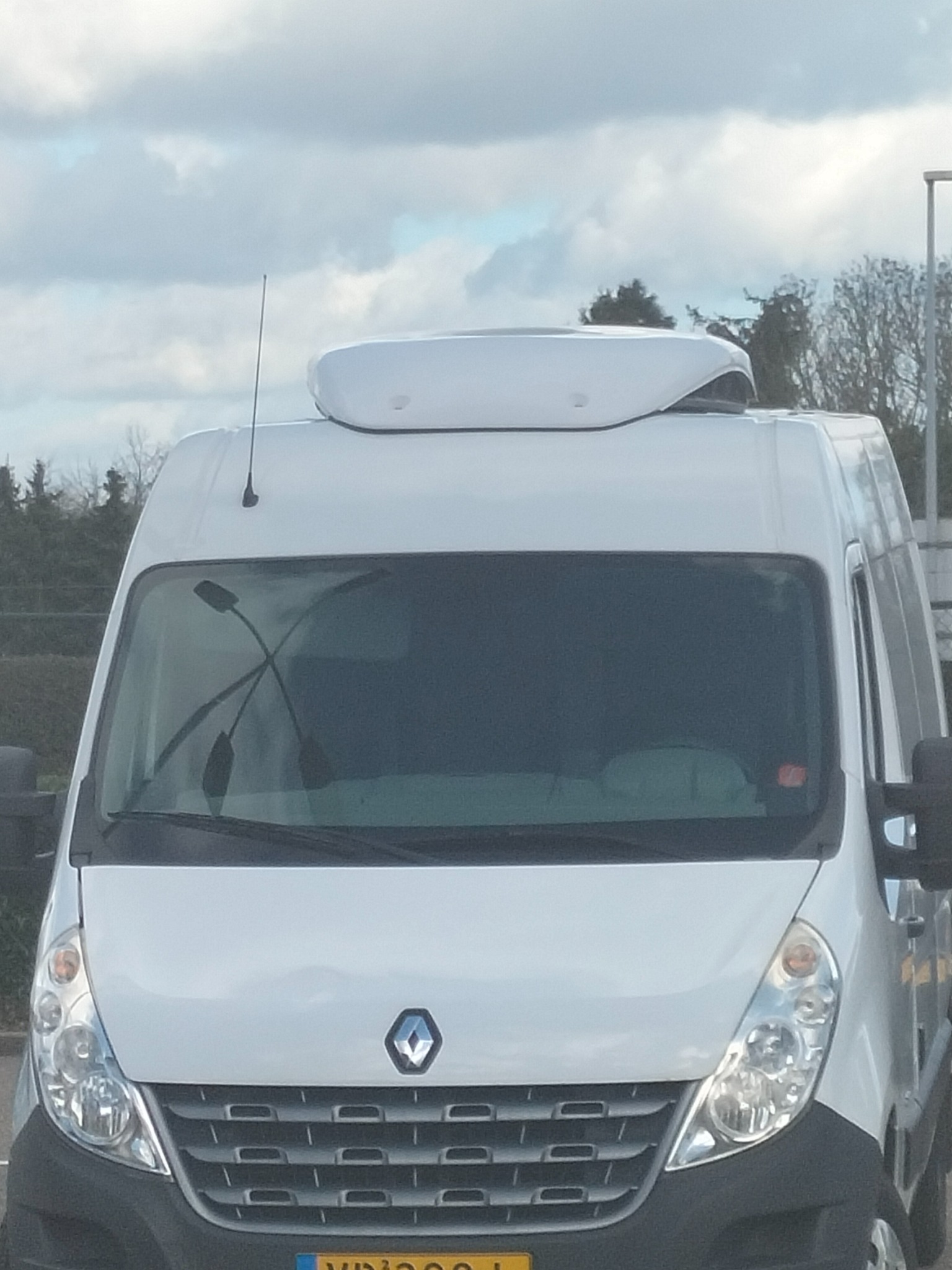 Przód białego Renault Master z agregatem chłodniczym na dachu, zaparkowany na zewnątrz w pochmurny dzień.