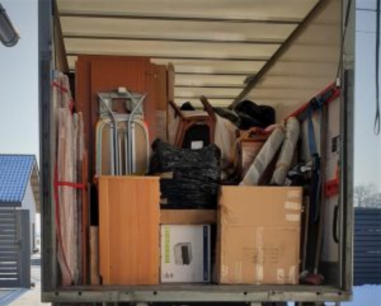 Wnętrze furgonetki załadowane meblami i kartonami podczas przeprowadzki, zabezpieczone pasami transportowymi, widoczne elementy wyposażenia domu.