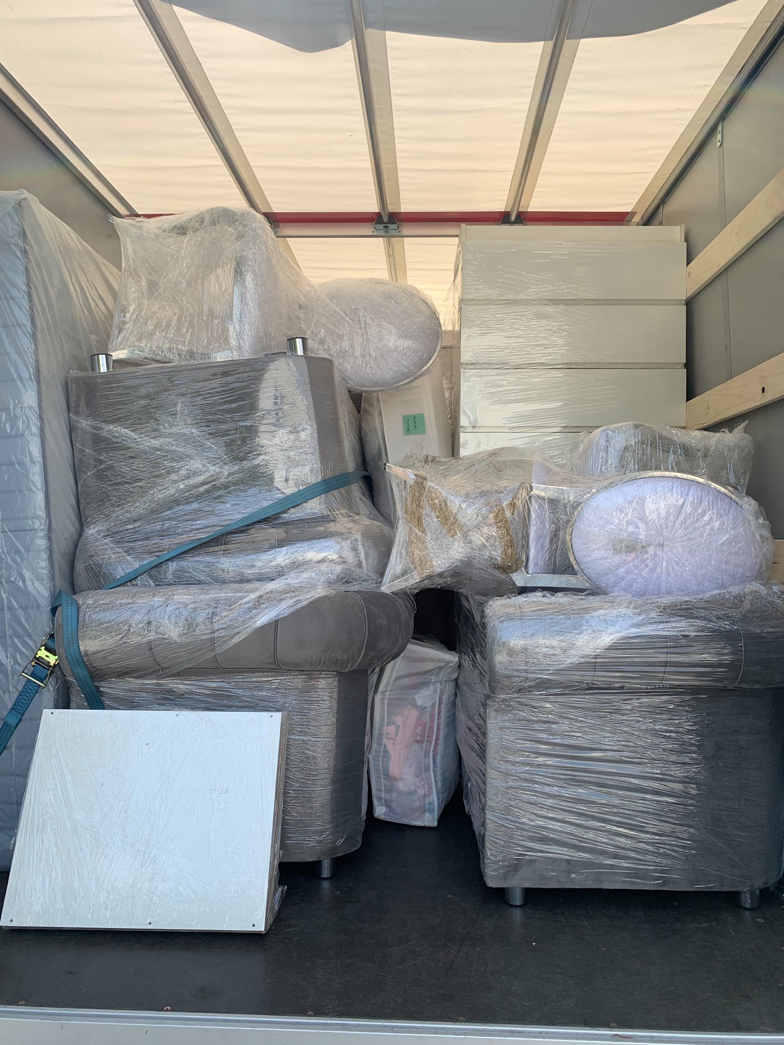 Wnętrze busa załadowane meblami (sofa, krzesła, szafki) owiniętymi folią stretch i zabezpieczonymi pasami transportowymi, gotowe do przewozu.