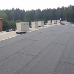 Wykończony dach pokryty papą termozgrzewalną w Radomsku, z kominami wentylacyjnymi i rolkami papy czekającymi na montaż.