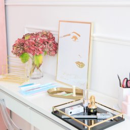 Katarzyna von Engel - makijaż permanentny brwi (microblading) Warszawa - Białe biurko kosmetyczne z akcesoriami do makijażu brwi: pęsety, nici, pigmenty, miarka i ramka ze złotym rysunkiem twarzy z perfekcyjnymi brwiami.