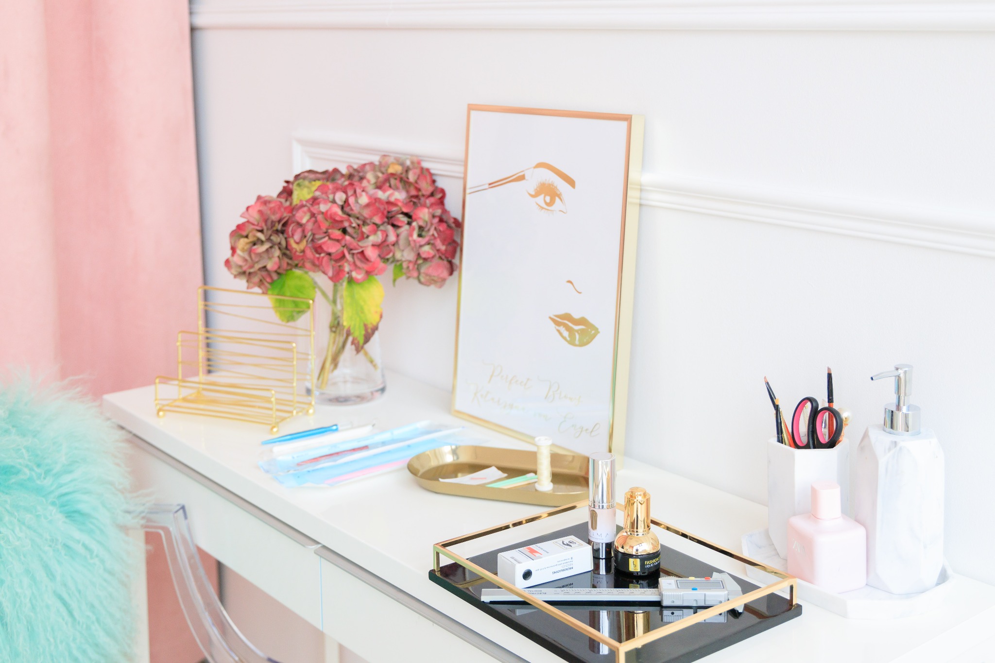 Białe biurko kosmetyczne z akcesoriami do makijażu brwi: pęsety, nici, pigmenty, miarka i ramka ze złotym rysunkiem twarzy z perfekcyjnymi brwiami.