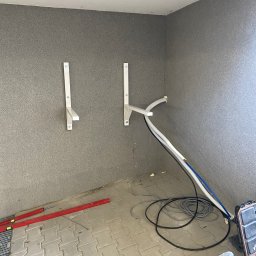 Mantex Instalacje - Przygotowanie do montażu klimatyzacji: wsporniki, przewody i narzędzia na podłodze w szarym pomieszczeniu. Etap instalacji przed montażem jednostki zewnętrznej.