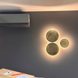 Mantex Instalacje - Nowoczesny klimatyzator ścienny LG na szarej ścianie z dekoracyjnym oświetleniem. Częściowo widoczny karton z akcesoriami montażowymi na dole kadru.